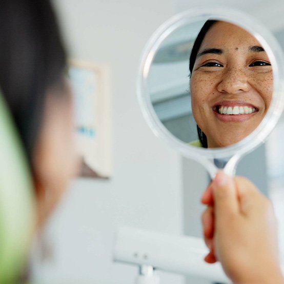 Woman smiling at reflection in handheld mirror