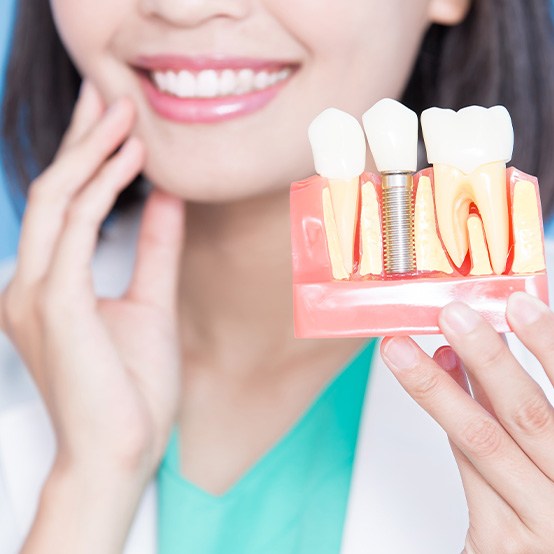 Nose-to-chest view of dentist in white coat holding up sample dental implant