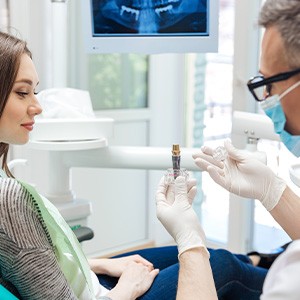 Dentist showing sample implant to woman in dental chair