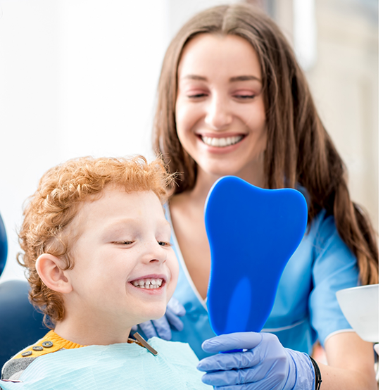 Dental team member holding mirror in front of smiling child in dental chair