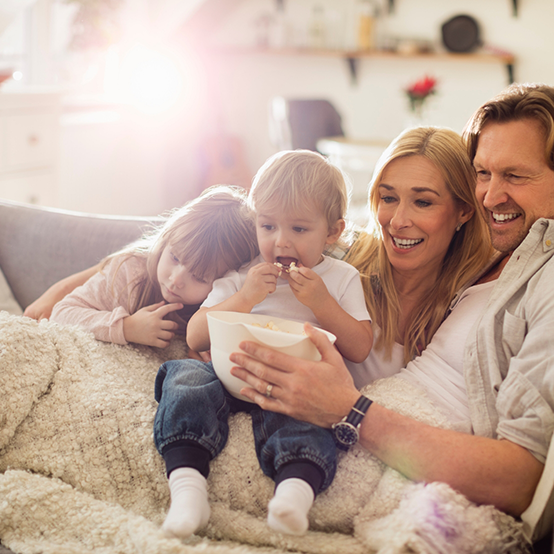 Family of four sitting on couch with bowl of popcorn