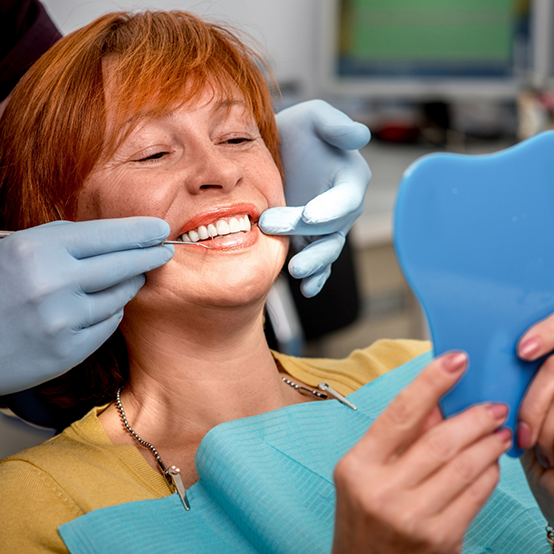 Woman in dental chair admiring her smile in mirror