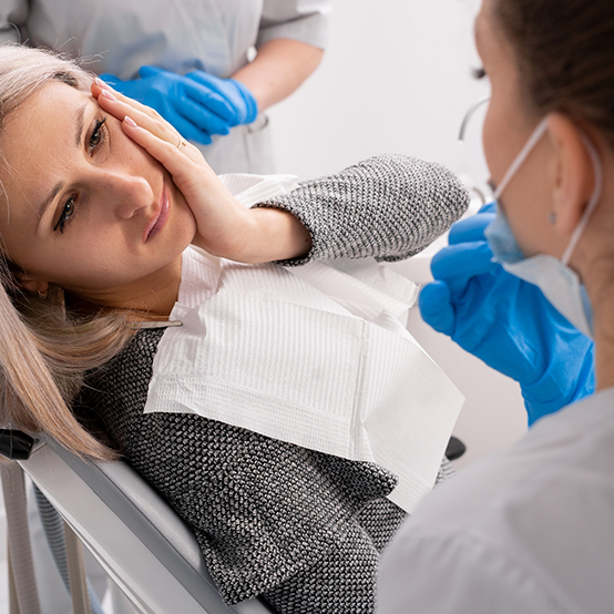 Woman holding her jaw in pain while talking to emergency dentist in Jupiter