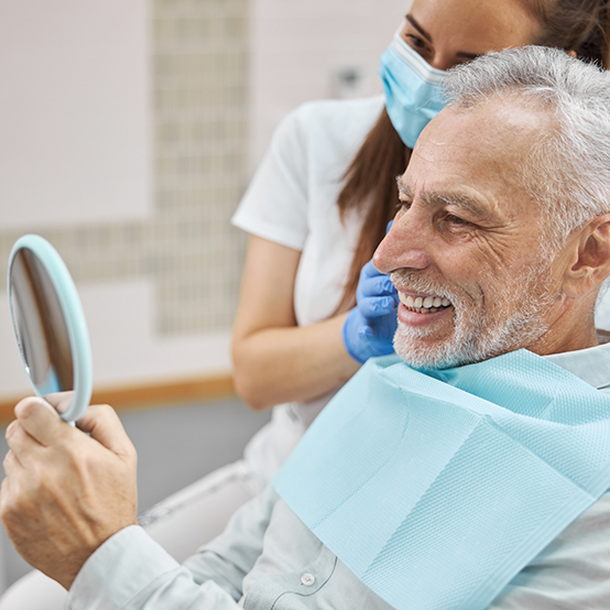 Senior dental patient admiring his smile in mirror