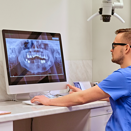 Dentist looking at computer showing x rays of patient with dental implants