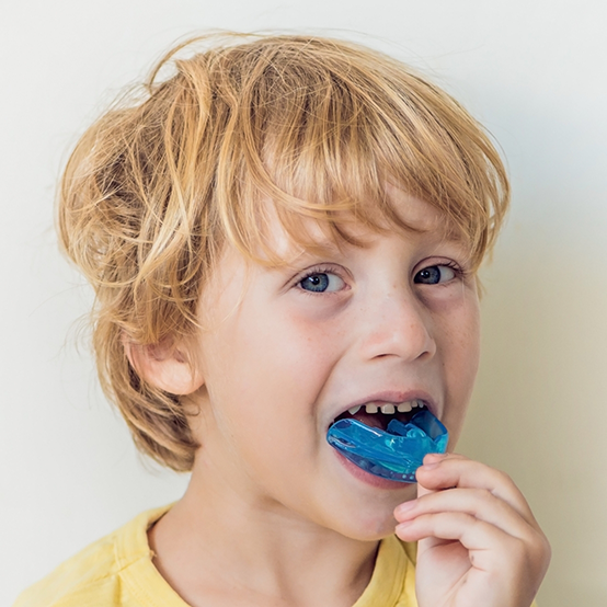 Boy placing a blue mouthguard over his teeth