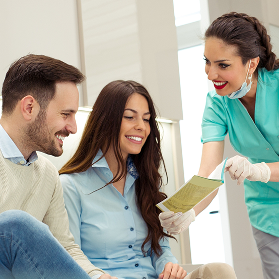 Dental team member showing a pamphlet to two patients